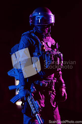 Image of Army soldier in Combat Uniforms with an assault rifle and combat helmet night mission dark background. Blue and purple gel light effect.