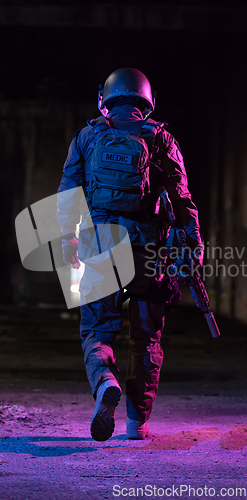 Image of Army soldier in Combat Uniforms with an assault rifle and combat helmet night mission dark background. Blue and purple gel light effect.