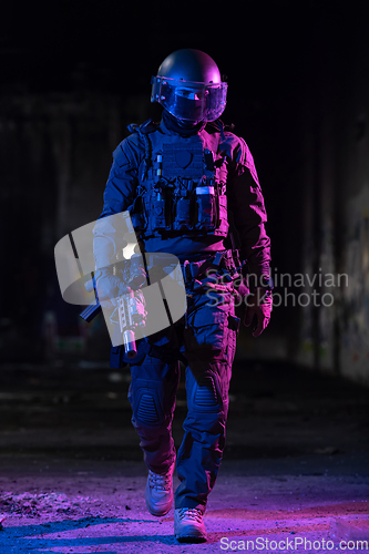 Image of Army soldier in Combat Uniforms with an assault rifle and combat helmet night mission dark background. Blue and purple gel light effect.