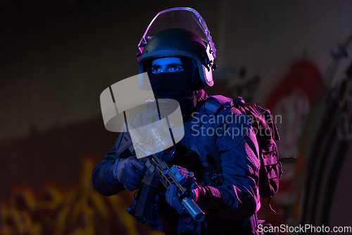 Image of Army soldier in Combat Uniforms with an assault rifle and combat helmet night mission dark background. Blue and purple gel light effect.