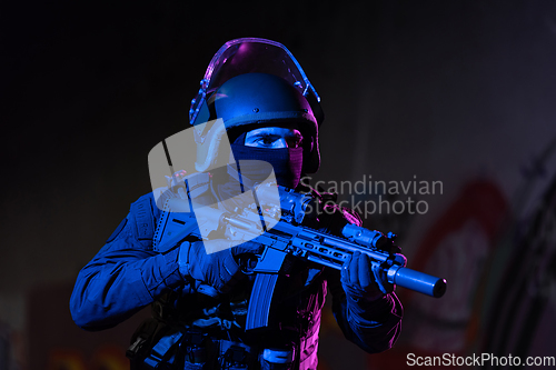 Image of Army soldier in Combat Uniforms with an assault rifle and combat helmet night mission dark background. Blue and purple gel light effect.