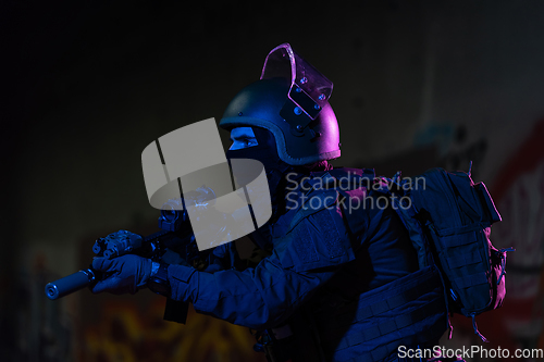 Image of Army soldier in Combat Uniforms with an assault rifle and combat helmet night mission dark background. Blue and purple gel light effect.