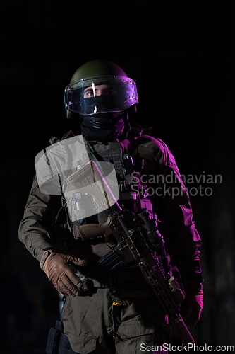 Image of Army soldier in Combat Uniforms with an assault rifle and combat helmet night mission dark background. Blue and purple gel light effect.