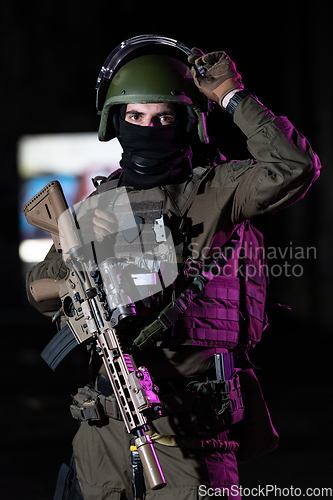 Image of Army soldier in Combat Uniforms with an assault rifle and combat helmet night mission dark background. Blue and purple gel light effect.