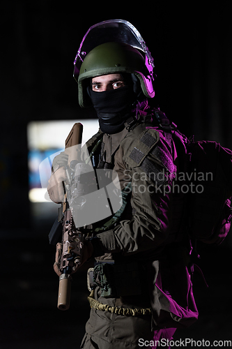 Image of Army soldier in Combat Uniforms with an assault rifle and combat helmet night mission dark background. Blue and purple gel light effect.