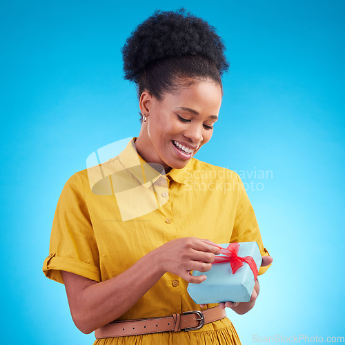 Image of Happy, gift and a black woman in studio with a surprise for birthday, celebration or holiday. Fashion, present and african female person on a blue background with a box, ribbon and prize or package