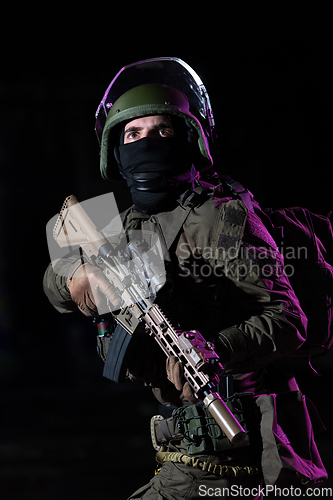 Image of Army soldier in Combat Uniforms with an assault rifle and combat helmet night mission dark background. Blue and purple gel light effect.