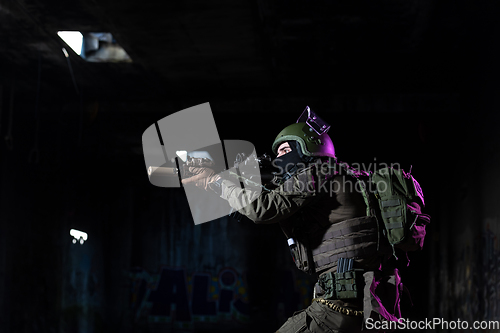 Image of Army soldier in Combat Uniforms with an assault rifle and combat helmet night mission dark background. Blue and purple gel light effect.