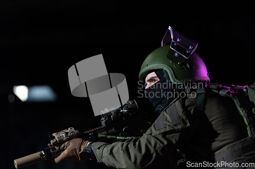 Image of Army soldier in Combat Uniforms with an assault rifle and combat helmet night mission dark background. Blue and purple gel light effect.