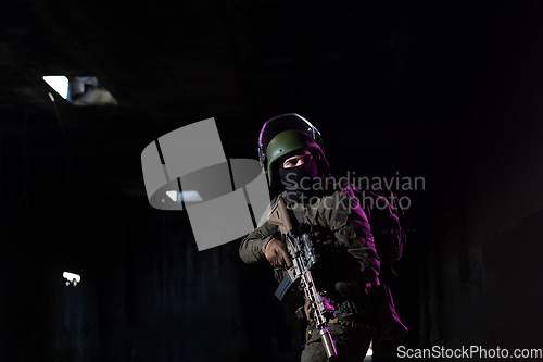 Image of Army soldier in Combat Uniforms with an assault rifle and combat helmet night mission dark background. Blue and purple gel light effect.