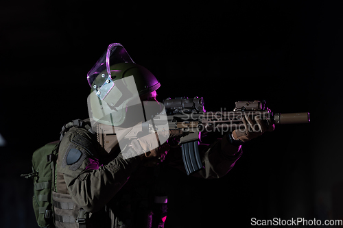 Image of Army soldier in Combat Uniforms with an assault rifle and combat helmet night mission dark background. Blue and purple gel light effect.