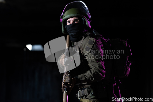 Image of Army soldier in Combat Uniforms with an assault rifle and combat helmet night mission dark background. Blue and purple gel light effect.