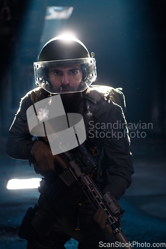 Image of Army soldier in Combat Uniforms with an assault rifle and combat helmet night mission dark background. Blue and purple gel light effect.