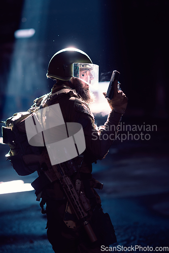 Image of Army soldier in Combat Uniforms with an assault rifle and combat helmet night mission dark background. Blue and purple gel light effect.