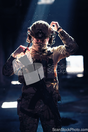 Image of Army soldier in Combat Uniforms with an assault rifle and combat helmet night mission dark background. Blue and purple gel light effect.