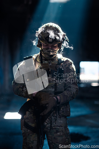 Image of Army soldier in Combat Uniforms with an assault rifle and combat helmet night mission dark background. Blue and purple gel light effect.