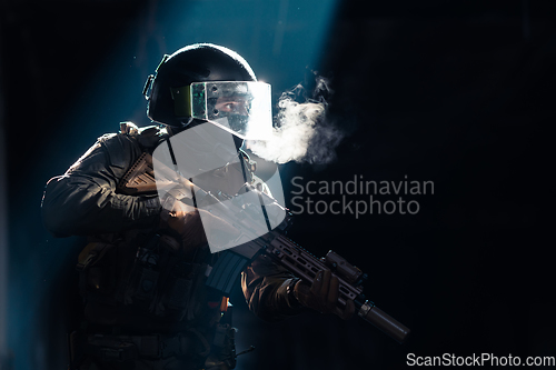 Image of Army soldier in Combat Uniforms with an assault rifle and combat helmet night mission dark background. Blue and purple gel light effect.