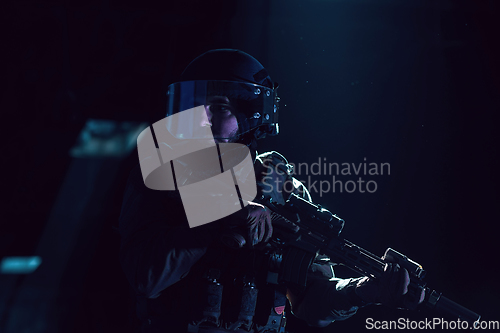 Image of Army soldier in Combat Uniforms with an assault rifle and combat helmet night mission dark background. Blue and purple gel light effect.