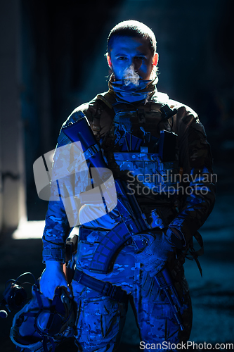 Image of Army soldier in Combat Uniforms with an assault rifle and combat helmet night mission dark background. Blue and purple gel light effect.