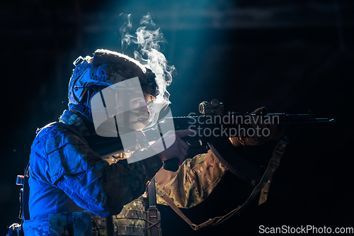 Image of Army soldier in Combat Uniforms with an assault rifle and combat helmet night mission dark background. Blue and purple gel light effect.