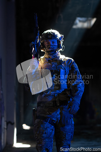 Image of Army soldier in Combat Uniforms with an assault rifle and combat helmet night mission dark background. Blue and purple gel light effect.