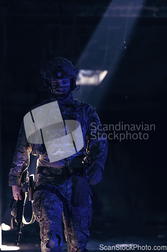 Image of Army soldier in Combat Uniforms with an assault rifle and combat helmet night mission dark background. Blue and purple gel light effect.