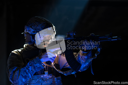 Image of Army soldier in Combat Uniforms with an assault rifle and combat helmet night mission dark background. Blue and purple gel light effect.