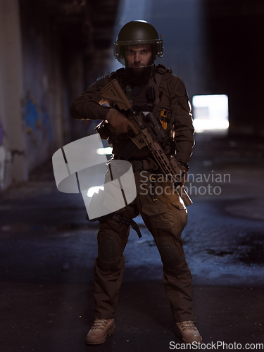 Image of Army soldier in Combat Uniforms with an assault rifle and combat helmet night mission dark background. Blue and purple gel light effect.