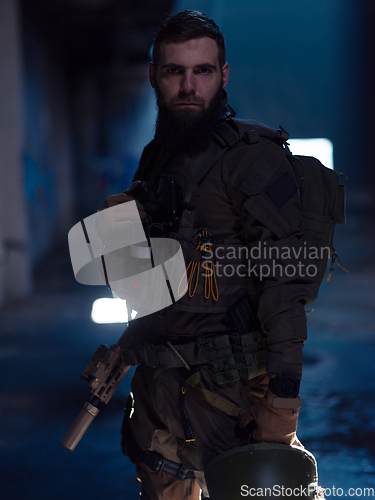 Image of Army soldier in Combat Uniforms with an assault rifle and combat helmet night mission dark background. Blue and purple gel light effect.