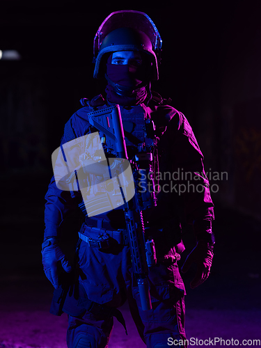 Image of Army soldier in Combat Uniforms with an assault rifle and combat helmet night mission dark background. Blue and purple gel light effect.