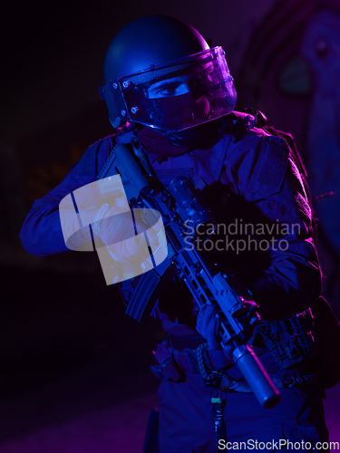 Image of Army soldier in Combat Uniforms with an assault rifle and combat helmet night mission dark background. Blue and purple gel light effect.