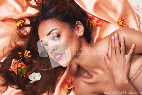 Image of Woman, flowers and makeup for portrait, floor or silk fabric for aesthetic, fashion or beauty in studio. Girl, model and face with plants, natural glow or relax with sustainable cosmetics in top view