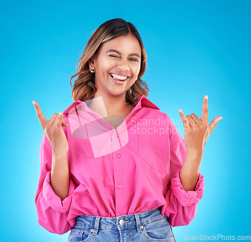 Image of Wink, portrait and woman with rocker hands in studio for freedom, happy and positive attitude on blue background. Smile, face and female with rockstar emoji, sign or punk gesture, good mood or vibes
