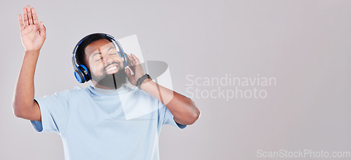 Image of Headphones, happy and young man in a studio listening to music, playlist or album while dancing. Happiness, smile and African male model streaming song or radio by gray background with mock up space.
