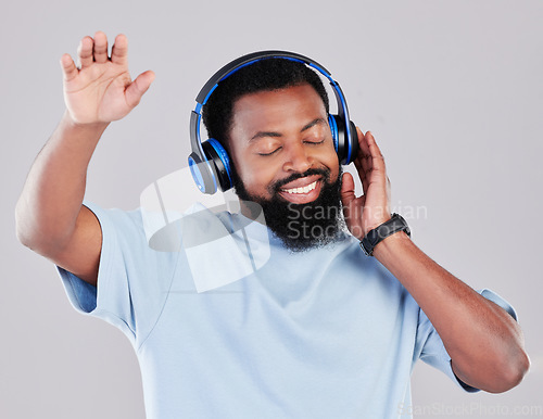 Image of Headphones, dance and man in a studio with music, playlist or album with a calm mindset. Happy, smile and young African male model streaming a song or radio online isolated by a gray background.