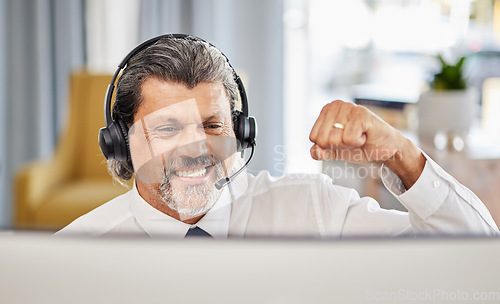 Image of Call centre, happy and a man at computer to celebrate success, achievement or bonus win. A mature male consultant or agent with a fist for customer service, help desk and crm or telemarketing target
