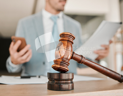 Image of Closeup, gavel and law firm on table, office or attorney man in blurred background, phone texting or networking. Advocate, lawyer or judge with legal hammer, reading and documents for court evidence