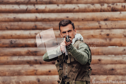 Image of A soldier in uniform with a rifle in his hand is standing in front of a wooden wall. A soldier guards the forest base from the enemy