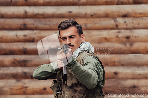 Image of A soldier in uniform with a rifle in his hand is standing in front of a wooden wall. A soldier guards the forest base from the enemy