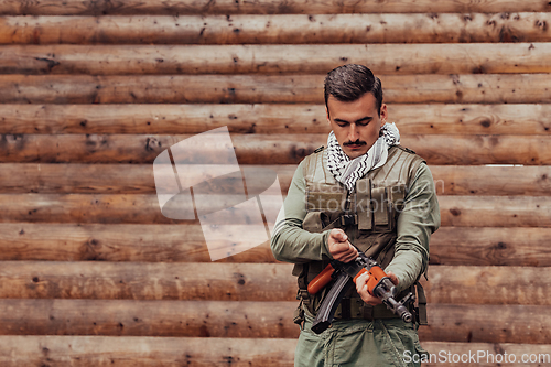 Image of A soldier in uniform with a rifle in his hand is standing in front of a wooden wall. A soldier guards the forest base from the enemy