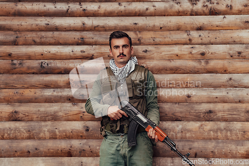 Image of A soldier in uniform with a rifle in his hand is standing in front of a wooden wall. A soldier guards the forest base from the enemy