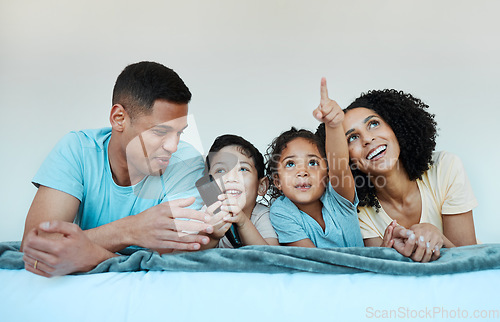 Image of Father, mom and kids on bed, watching tv and smile for comedy, funny movie or pointing in family home. Happy parents, children and watch television show with streaming, subscription or laugh together