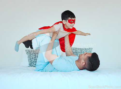 Image of Airplane, bedroom and dad playing with his kid for bonding, fun or happiness at their home. Happy, smile and young father relaxing with his boy child in a superhero costume on the bed at family house