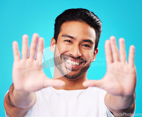 Image of Portrait, hands and man frame face in studio to review profile picture on blue background. Happy young asian model planning perspective of photography, selfie and creative inspiration for border sign