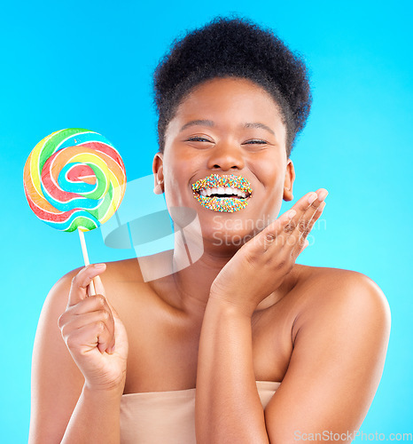 Image of Candy, portrait and woman with sprinkles on her lips in a studio with sweet treats, dessert or snack. Happy, smile and young African female model with a colorful lollipop isolated by blue background.