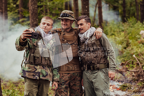 Image of Team of soldiers and terrorist taking selfie with smartphone in the forest