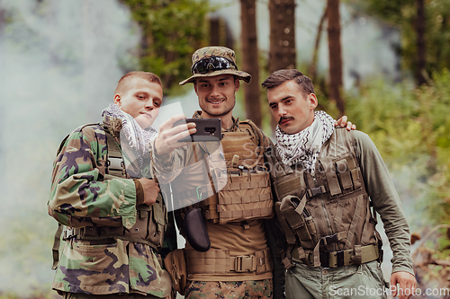 Image of Team of soldiers and terrorist taking selfie with smartphone in the forest