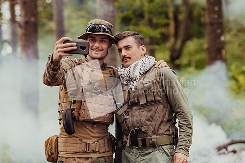 Image of Team of soldiers and terrorist taking selfie with smartphone in the forest