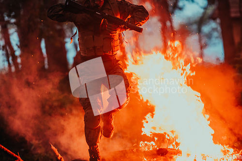 Image of Soldier in Action at Night in the Forest Area. Night Time Military Mission jumping over fire