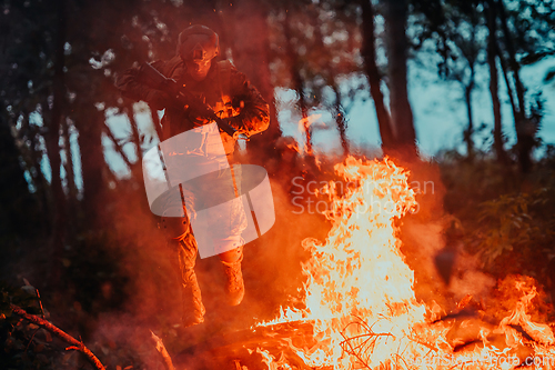 Image of Soldier in Action at Night in the Forest Area. Night Time Military Mission jumping over fire